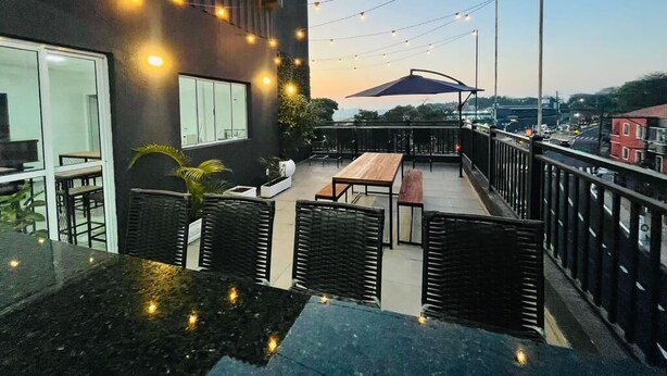 An outdoor patio with tables and chairs, string lights, and a view of the cityscape.