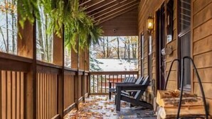 Une véranda en bois avec un banc et une table, recouverts de feuilles mortes, et une vue sur un paysage enneigé.