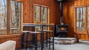 L’intérieur d’un chalet en bois est doté d’une cheminée en pierre, d’une table à manger avec des tabourets et de grandes fenêtres.