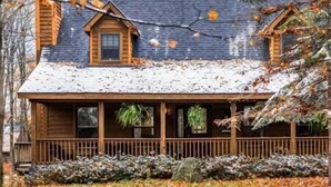 Une cabane en bois avec un toit enneigé, une véranda dotée de balustrades et une cheminée.
