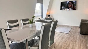 A modern dining area with a rectangular table, six chairs, a potted plant, and a flat-screen TV mounted on the wall.