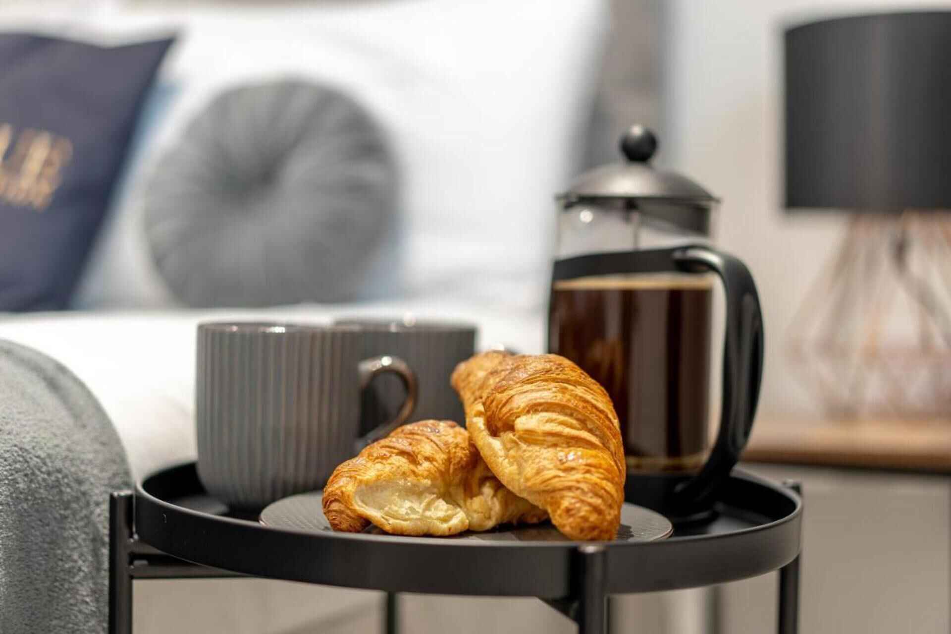 En bakke med croissanter og kaffepotte på et bord i et hotelværelse.