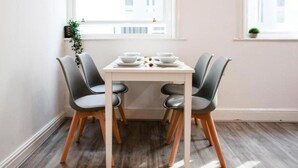 Une table à manger avec quatre chaises, une nappe blanche et une fenêtre avec une plante sur le rebord.
