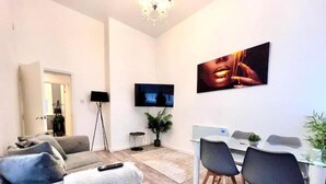 Un salon moderne comprenant un canapé, une table basse, une table à manger avec des chaises, un téléviseur et une plante.