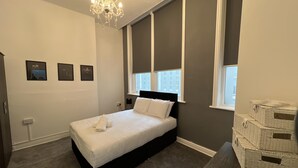 A bedroom with a large bed, a chandelier, a window with blinds, and a stack of baskets. - Lovely 2-bed Apartment in Liverpool (Liverpool)