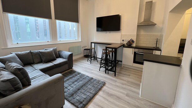 A modern living room with a grey sofa, a small rug, and a TV mounted on the wall. - Lovely 2-bed Apartment in Liverpool (Liverpool)