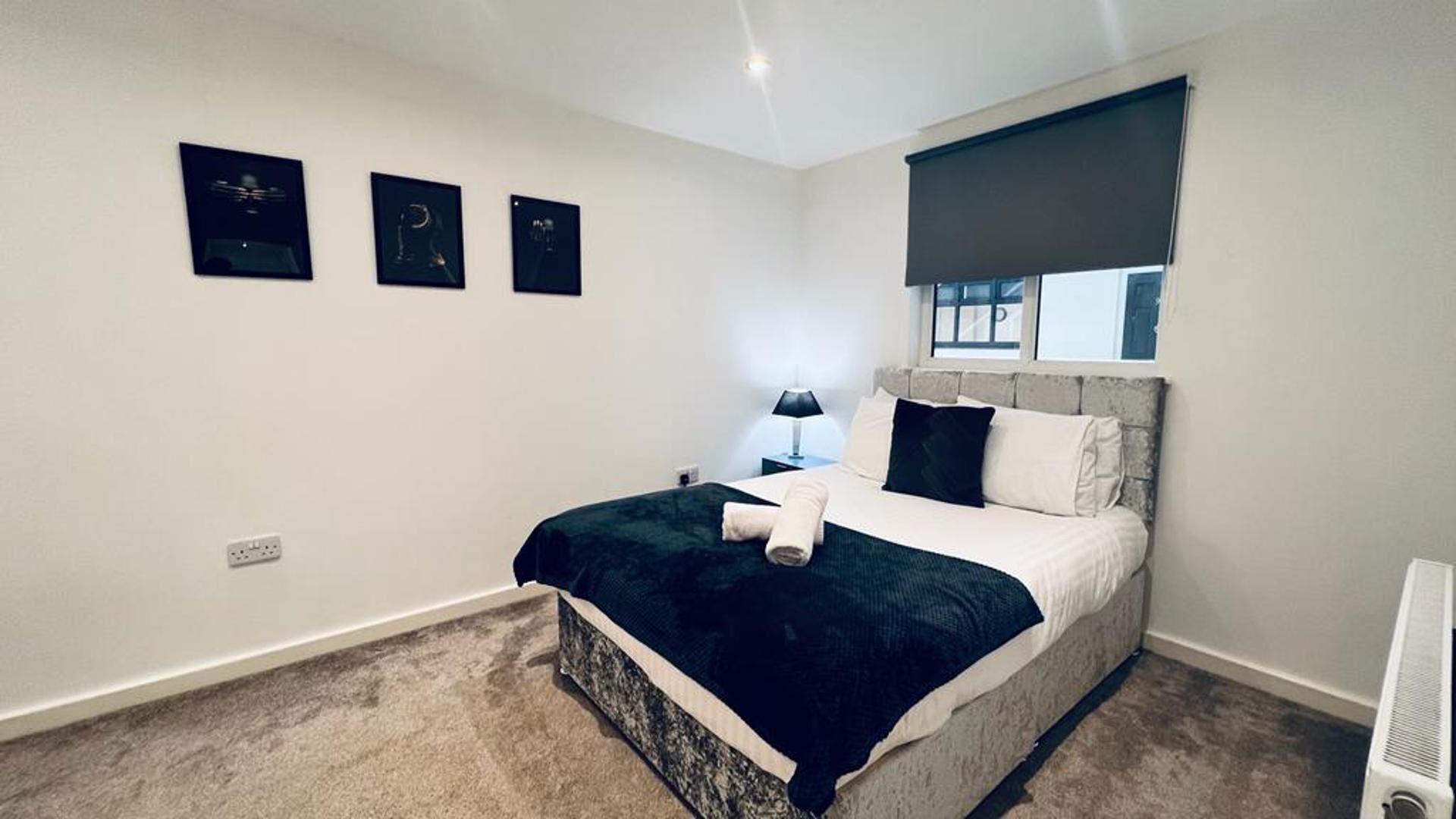 A bedroom with a bed, a nightstand, a lamp, and a window with a blind.