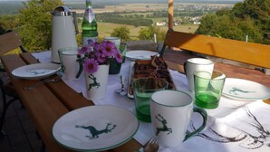 A table set outdoors with plates, cups, and a bottle, overlooking a scenic landscape. - Kellerstockl am Hamerlberg/strem (Strem)