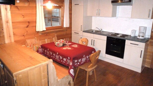 Una cocina compacta con gabinetes blancos, un lavavajillas negro y una mesa de comedor cubierta con mantel rojo.