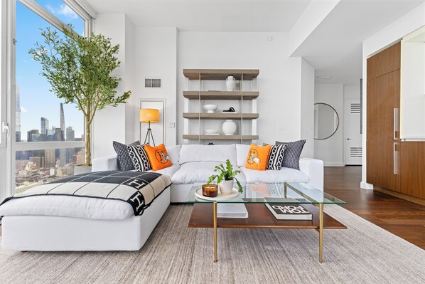 Ein modernes Wohnzimmer mit einem Glastisch, weißen Sofas und Blick auf die Stadt.