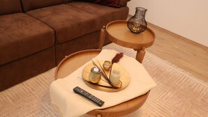 A small wooden side table with a remote control, a candle, and decorative items on a beige cloth. - City Apartment With Waterbed (Essen)