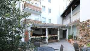 An outdoor patio area with a round table and chairs, a covered seating area with a railing, and a stone wall. - City Apartment With Waterbed (Essen)