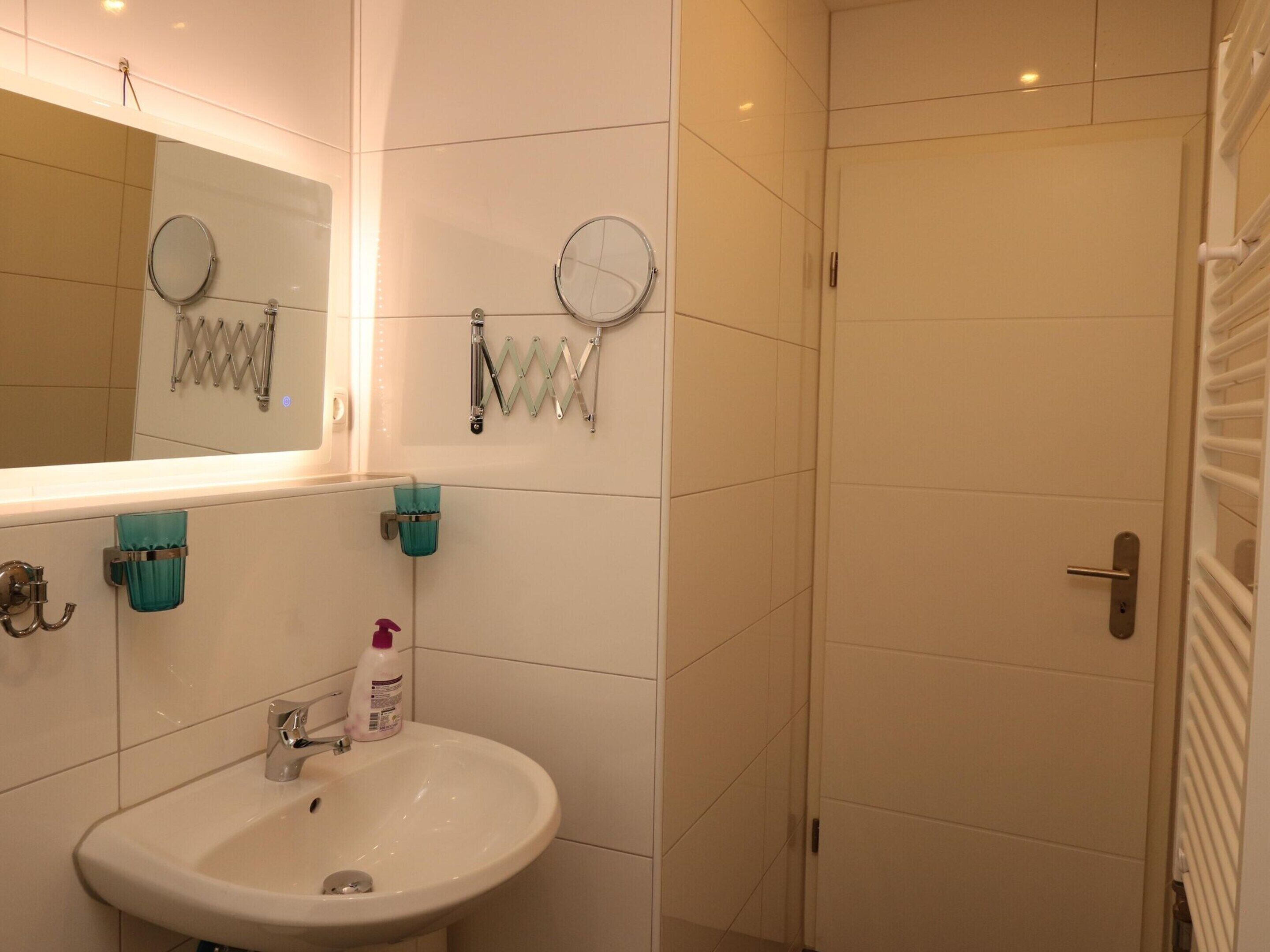 A bathroom with a sink, mirror, towel rack, and shower door.