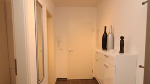 A narrow hallway with a white door at the end, a white cabinet with drawers, and two vases on top. - City Apartment With Waterbed (Essen)