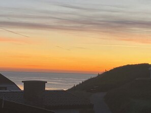 Une vue sur le coucher de soleil sur la côte, avec un bâtiment et une colline au premier plan.