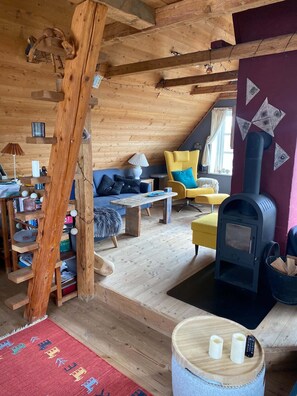 Interior acogedor de una cabaña con techo de madera, un sofá, un sillón amarillo, una mesa, una chimenea y una alfombra.