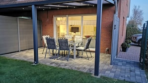 A covered patio with a table and chairs, a brick house, and a garage. - Dinkla 1 Comfortable Holiday Residence (Dornum)