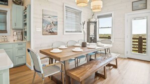 A dining area with a wooden table, white chairs, and a bench. There are three pendant lights hanging above the table. - Private Pool|Steps to Beach|Ocean View (Port Aransas)