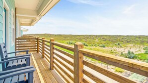 A wooden deck with a railing, two blue chairs, and a view of a hilly landscape. - Private Pool|Steps to Beach|Ocean View (Port Aransas)