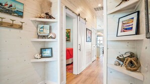 A hallway with wooden walls, a bed with a red blanket, and various decorative items on shelves. - Private Pool|Steps to Beach|Ocean View (Port Aransas)