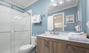 Un baño con cabina de ducha de vidrio, inodoro blanco, lavamanos con espejo y armarios de madera.