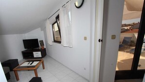 A small, well-lit room with a television, a small table, and a window with curtains. - LUANA One-Bedroom Apartment with Balcony (Rovinj)