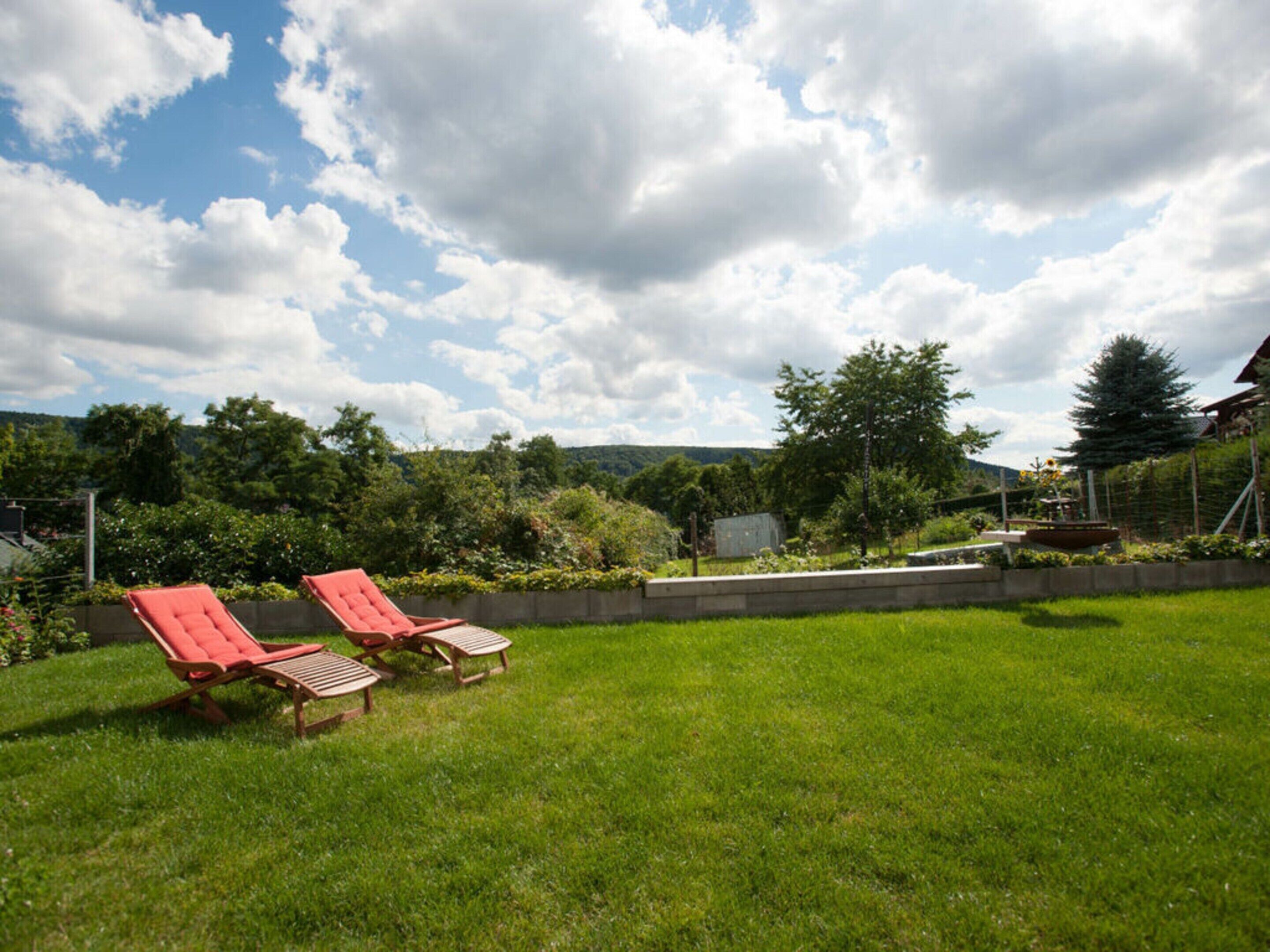 A grassy backyard with two red lounge chairs and a small table.