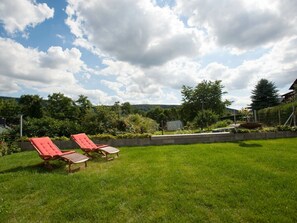 A grassy backyard with two red lounge chairs and a small table. - Holiday Home Foresight (Heilbad Heiligenstadt)
