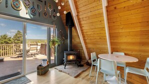 A cozy cabin interior with a wood stove, a deck with outdoor furniture, and a dining area with chairs and a table. - Indigo //Aframe- Hot Tub- Views! (Divide)
