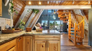 A wooden interior with a kitchen island, wooden cabinets, a spiral staircase, and a view of the outdoors. - Indigo //Aframe- Hot Tub- Views! (Divide)