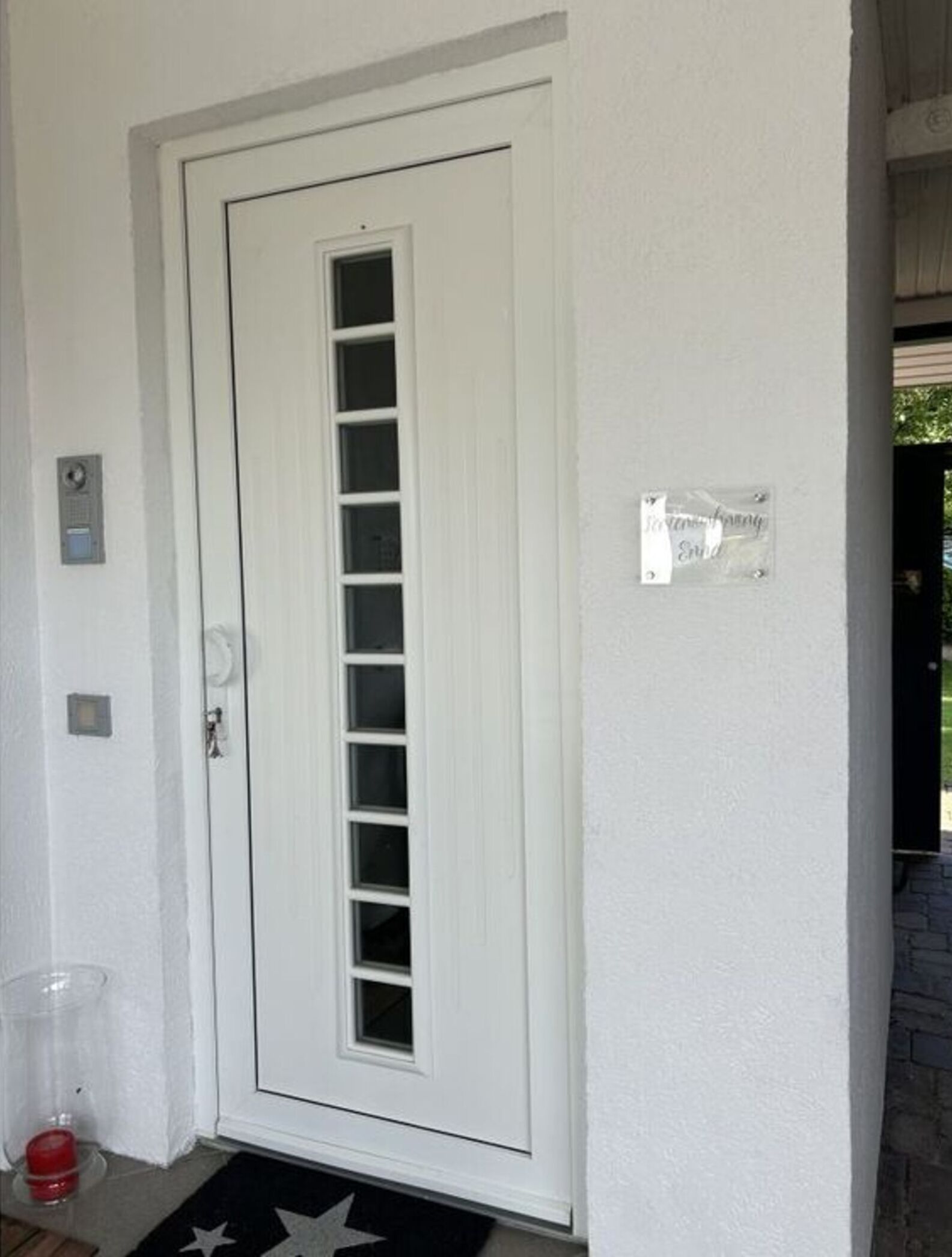 Une porte blanche avec une fenêtre verticale, une boîte aux lettres et une petite plaque fixée au mur.