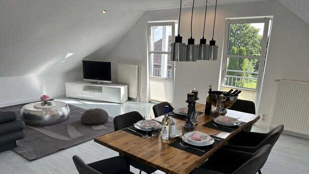 A modern dining area with a wooden table, black chairs, and a white cabinet with a television.