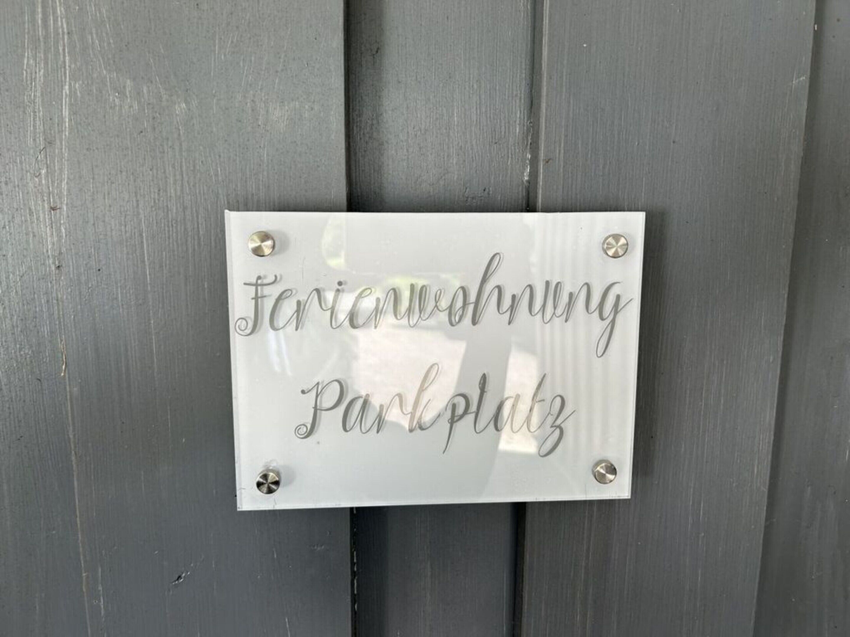 Harmaaseen puuseinään on kiinnitetty kyltti, jossa lukee ”Feriendorf” ja ”Parkplatz”.