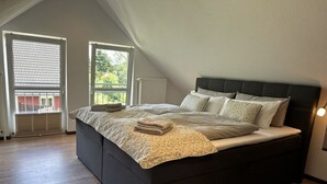 A modern bedroom with a large bed, a radiator, and a view of greenery through a window.