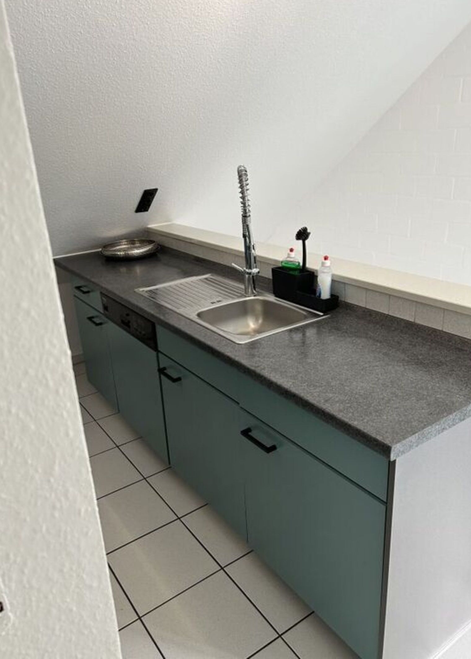 Una cocina con un lavamanos de acero inoxidable, un escurreplatos y un dispensador de jabón.
