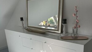 A white, modern dresser with a mirror and a vase of pink flowers.