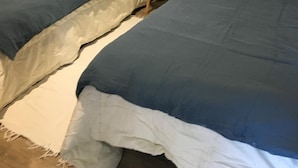 Un dormitorio con dos camas individuales, una mesita de noche pequeña con lámpara y una pared blanca.