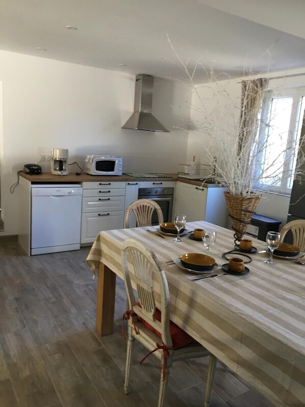 Compact kitchen with coffee maker, microwave, and stove, adjacent to a dining area with a table for two.