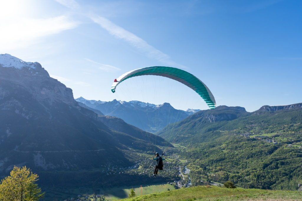 En person som skärmflyger över ett bergigt landskap under en klar himmel.
