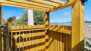Una terraza de madera con un cabezal de ducha, una toalla blanca y vista al mar.