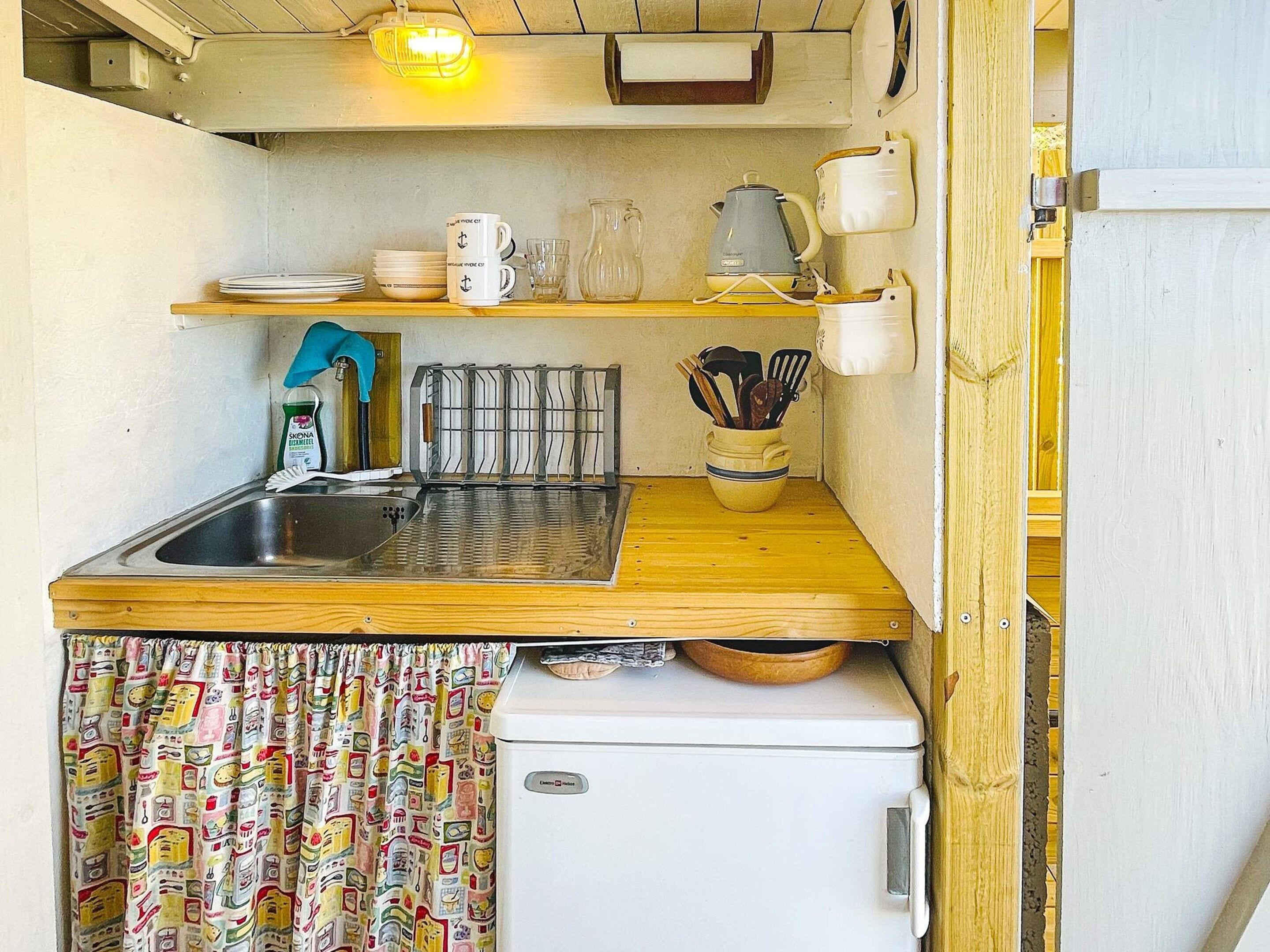 Een ruimtelijk ingerichte kitchenette met een spoelbak, een kleine koelkast en een houten aanrecht.