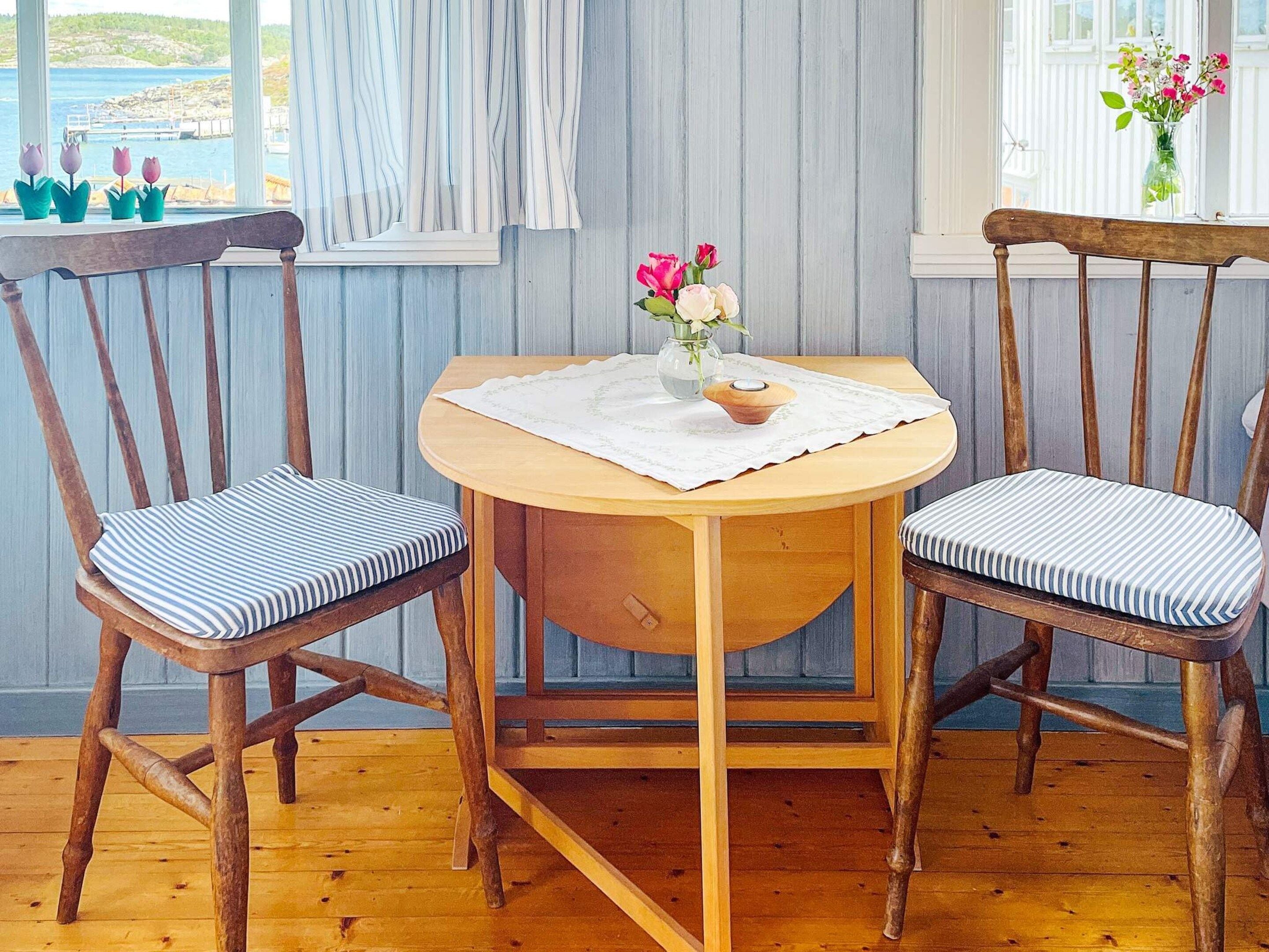 Una mesa de comedor de madera con dos sillas, un florero con flores y una ventana con cortinas.