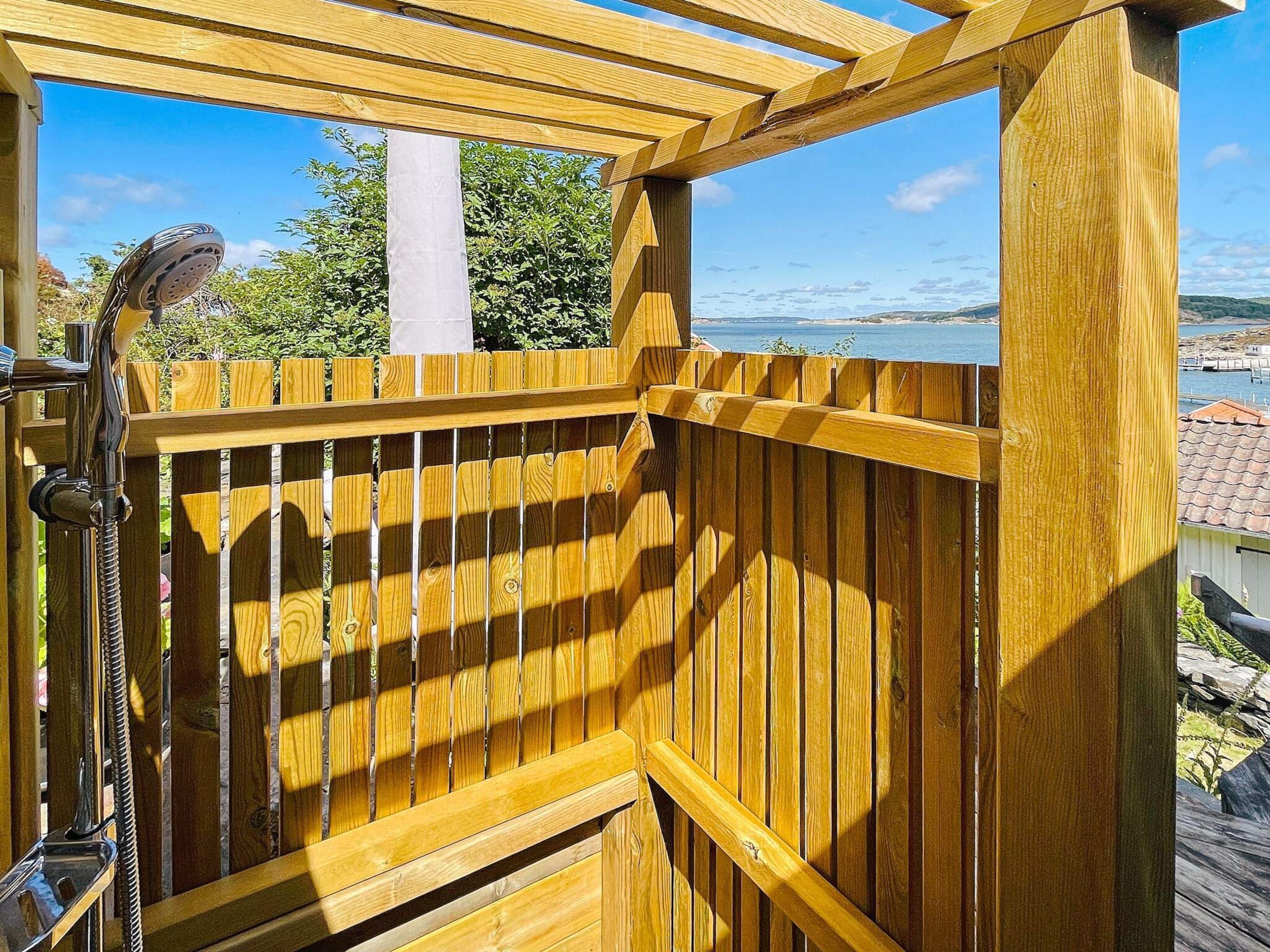 A wooden deck with a shower area, overlooking a body of water and a distant landscape.