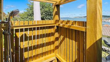 A wooden deck with a shower area, overlooking a body of water and a distant landscape.