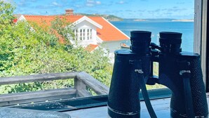 Binoculares sobre un alféizar con vista a una casa y al mar.