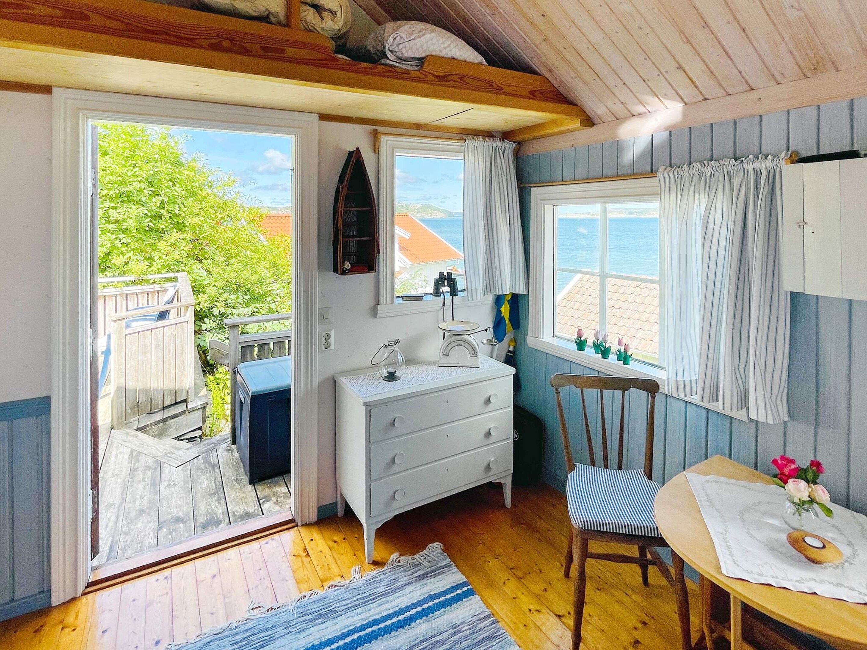 Een gezellige kamer met een houten vloer, een witte dressoir, een stoel en een raam met gordijnen.