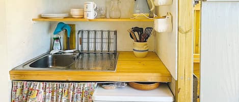 A compact kitchen with a sink, a small refrigerator, and a wooden countertop.