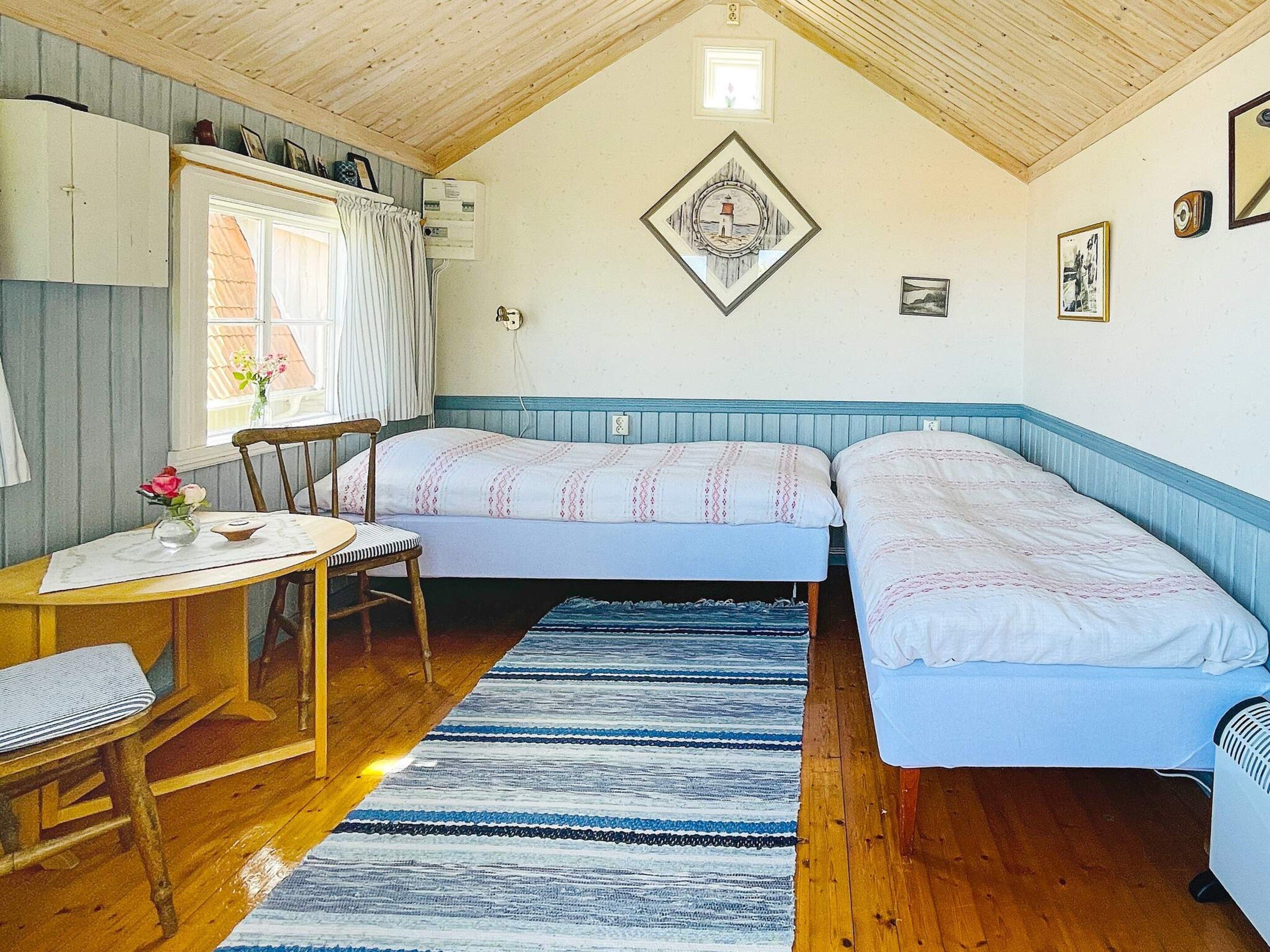 Une pièce avec un plafond en bois, un lit avec une tête de lit bleue, une petite table avec une chaise et une fenêtre avec des rideaux.