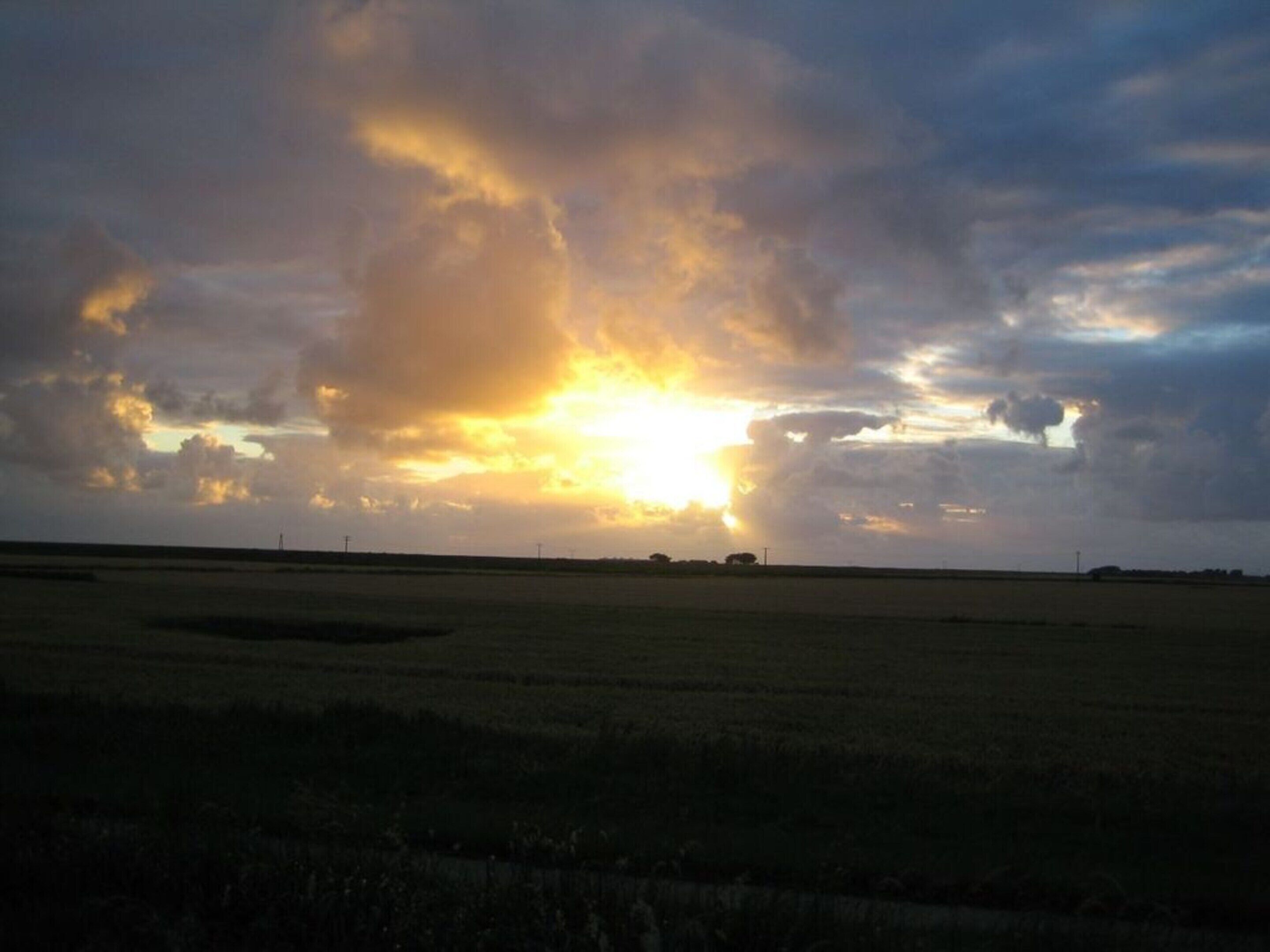 A flat landscape with a wide-open field and a cloudy sky.