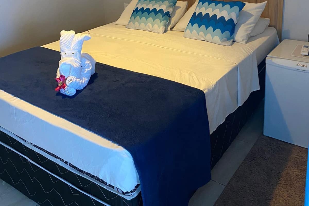 A neatly made bed with a blue and white patterned bedspread, a white pillow with a blue and white pattern, and a white stuffed animal on the bed.